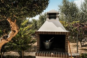 An outdoor brick oven with a chimney, surrounded by trees and a fence.