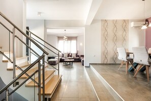 A modern living room with a staircase, a dining area with chairs, and a sofa.