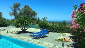 Un espace piscine avec des chaises longues bleues, une piscine en pierre et une vue sur la mer.