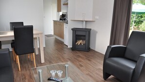 A modern living room with a glass coffee table, black leather chairs, a kitchen in the background, and a fireplace. - Chalet in Parc de Kievit with Private Garden (Baarle-Nassau)