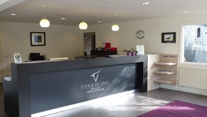 A reception desk with a logo, a clock, and a window with blinds. - Chalet in Parc de Kievit with Private Garden (Baarle-Nassau)