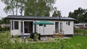 A single-story mobile home with a patio area, a green umbrella, and a small garden. - Chalet in Parc de Kievit with Private Garden (Baarle-Nassau)