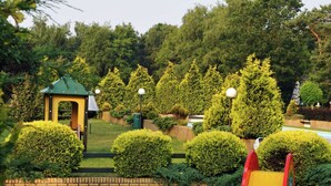 A swimming pool with a slide, surrounded by well-manicured bushes and trees. - Chalet in Parc de Kievit with Private Garden (Baarle-Nassau)