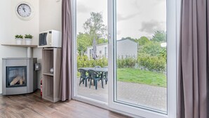 A room with a sliding glass door leading to a garden, a microwave, a small refrigerator, and a clock on the wall. - Chalet in Parc de Kievit with Private Garden (Baarle-Nassau)
