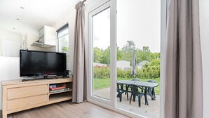 Una sala de estar moderna con un televisor de pantalla plana, un mueble de madera y un ventanal corredero que da a un patio exterior con mesa y sillas.