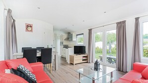 Una sala de estar moderna con un sofá rojo, una mesa de centro de vidrio y un televisor. Cuenta con un comedor con mesa y sillas, y una cocina con televisor y armarios.