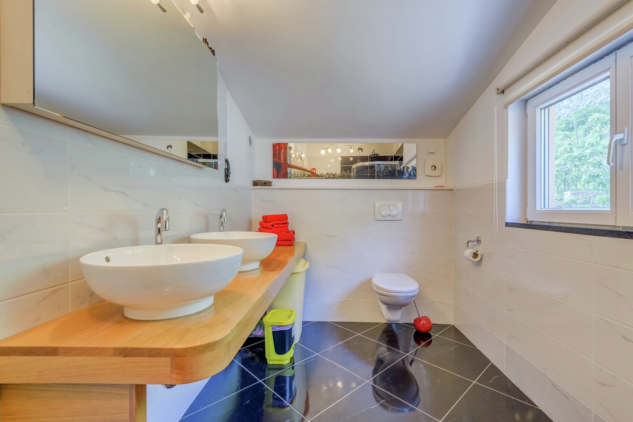 A modern bathroom with two sinks, a toilet, and a window.