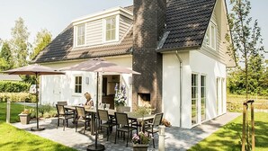 Une maison à deux étages dotée d’un patio comprenant une table et des chaises, une cheminée et un jardin.