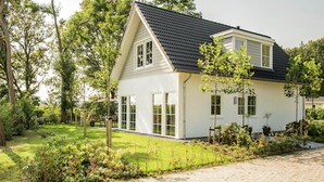 Une maison de plain-pied avec un toit sombre, des murs extérieurs blancs et de grandes fenêtres.