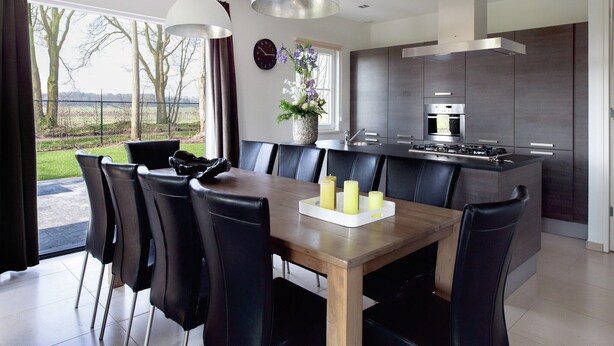 Une cuisine moderne avec des meubles de couleur sombre, un îlot central et un coin repas comprenant une table en bois et des chaises noires.