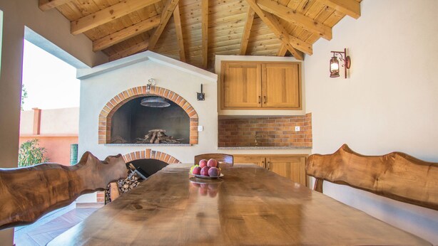 A wooden dining table with a brick oven, wooden cabinets, and a rustic ceiling.