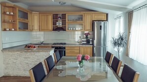 A modern kitchen with wooden cabinets, a central island, and a dining area with a glass table and chairs.