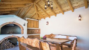 A rustic dining area with a wooden table and benches, a brick oven, and wooden beams on the ceiling.