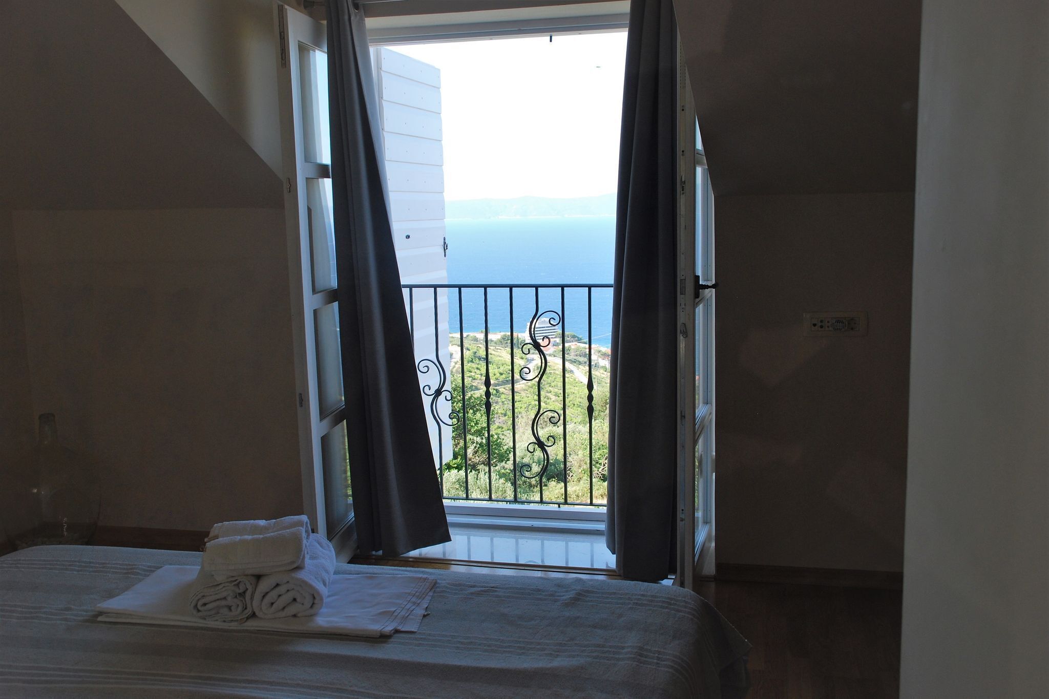 A hotel room with a bed, a window with curtains, and a view of the sea.