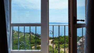 Un balcon doté d’une rambarde en métal, une vue sur la mer et un paysage verdoyant avec un sentier.