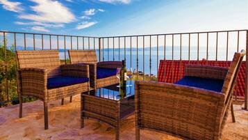 Des meubles en osier agrémentés de coussins, une table en verre et une vue sur la mer.