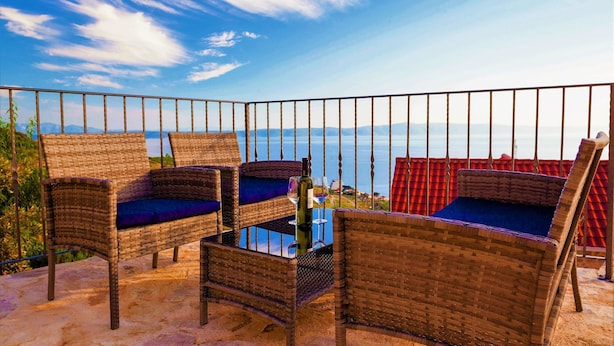 Wicker furniture with cushions, a glass table, and a view of the sea.