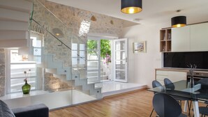 A modern interior with a staircase leading to a balcony, a dining area with a glass table, and a kitchen with a TV.