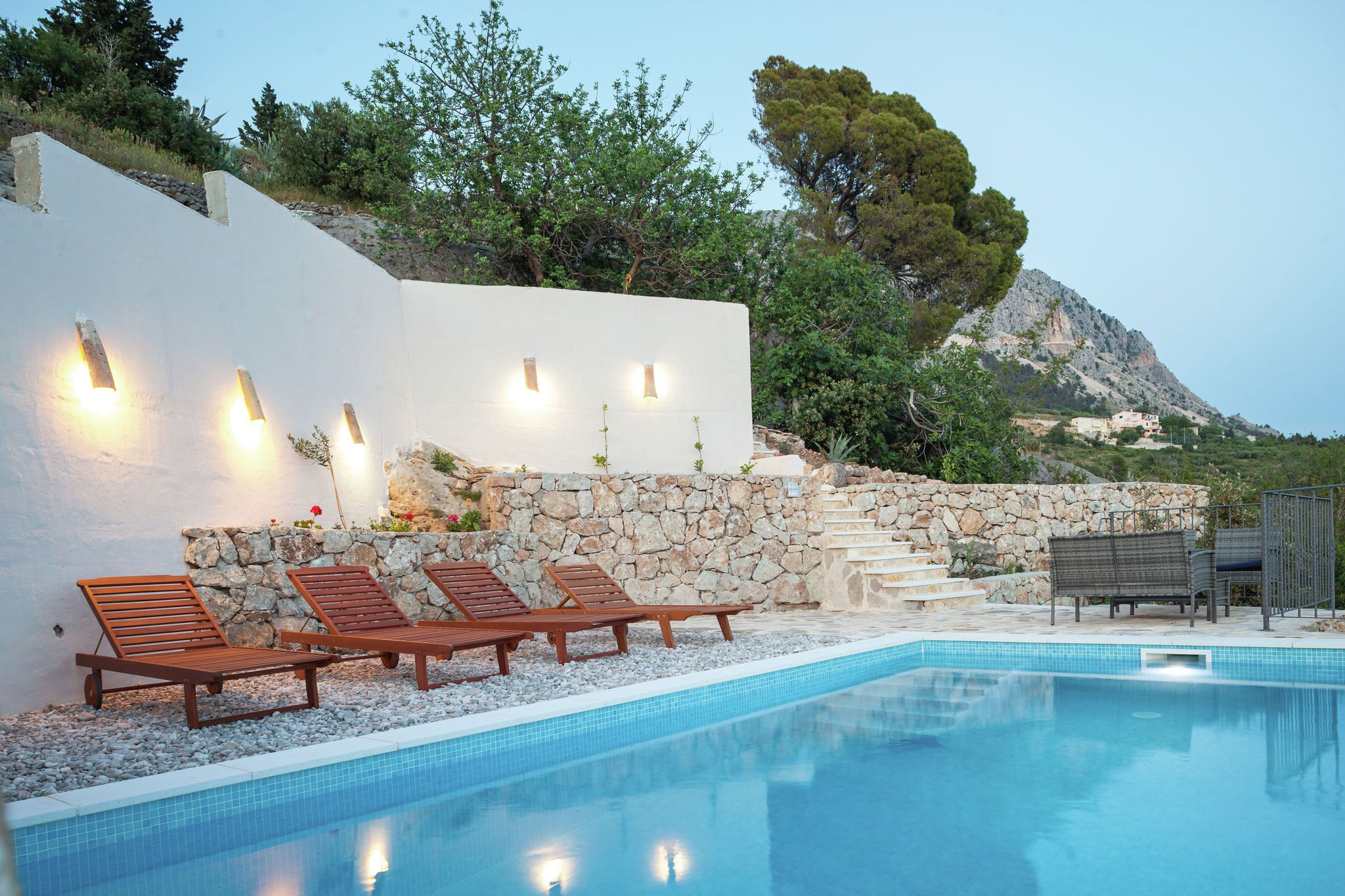 Un espace piscine avec des chaises longues, un mur en pierre et une vue sur la montagne.