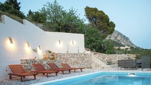 A pool area with lounge chairs, a stone wall, and a mountain view.