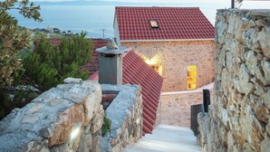 A stone staircase leading to a building with a red-tiled roof, surrounded by greenery and overlooking a body of water.