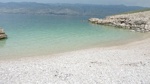 A pebble beach with clear water and distant mountains.