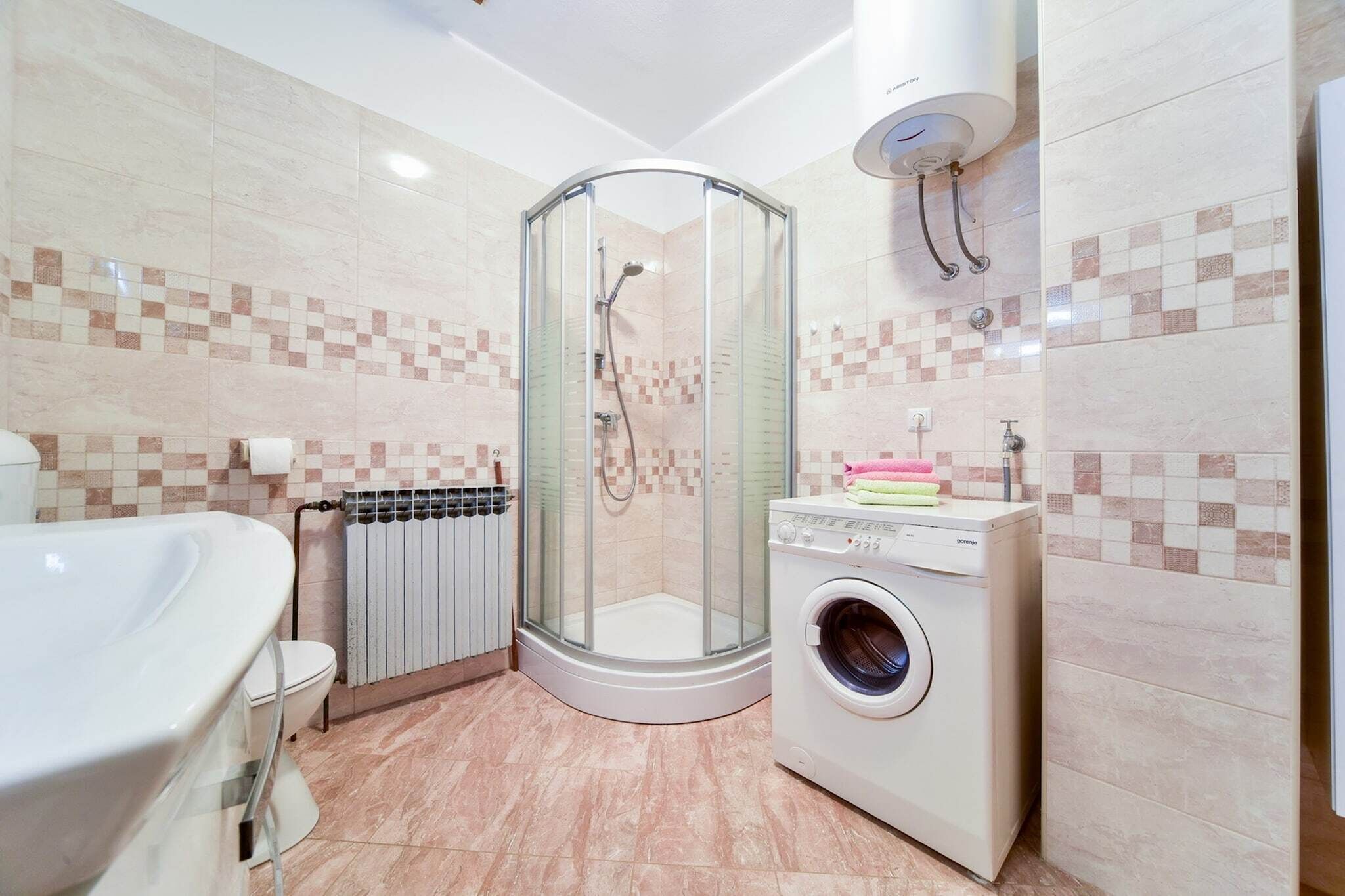 Une salle de bain moderne dotée d’une douche à parois de verre, d’une baignoire blanche, d’un lave-linge encastré et d’un pare-feu en carrelage.