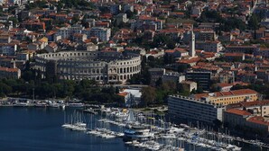 Un paisaje urbano costero con un edificio histórico, un puerto deportivo con numerosas embarcaciones y edificios residenciales muy juntos.