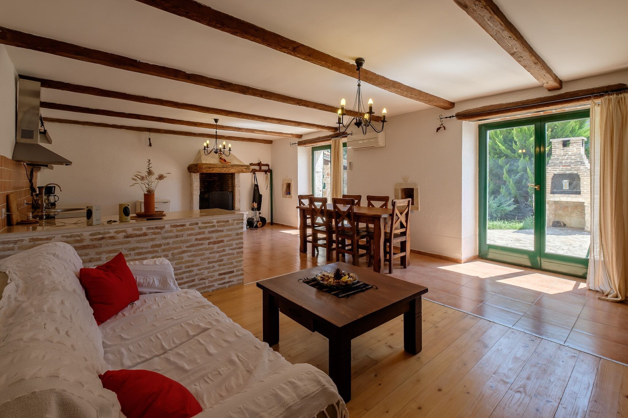 A spacious living area with a wooden floor, a sofa with red cushions, a dining table, and a fireplace.