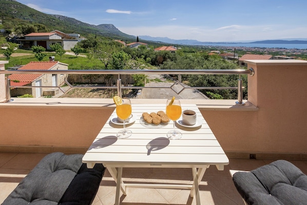 A balcony with a table set for breakfast, overlooking a scenic landscape with houses and mountains. - Sea-View Retreat, Kastel (Kastel Stari)