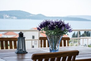 A table with a vase of flowers and a lantern, overlooking a body of water with distant hills.