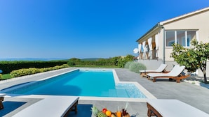 Una piscina con sillas de descanso, una cesta de frutas y vistas al paisaje.