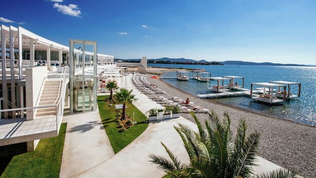 Un hotel moderno con zona de piscina, asientos exteriores y vistas al mar.