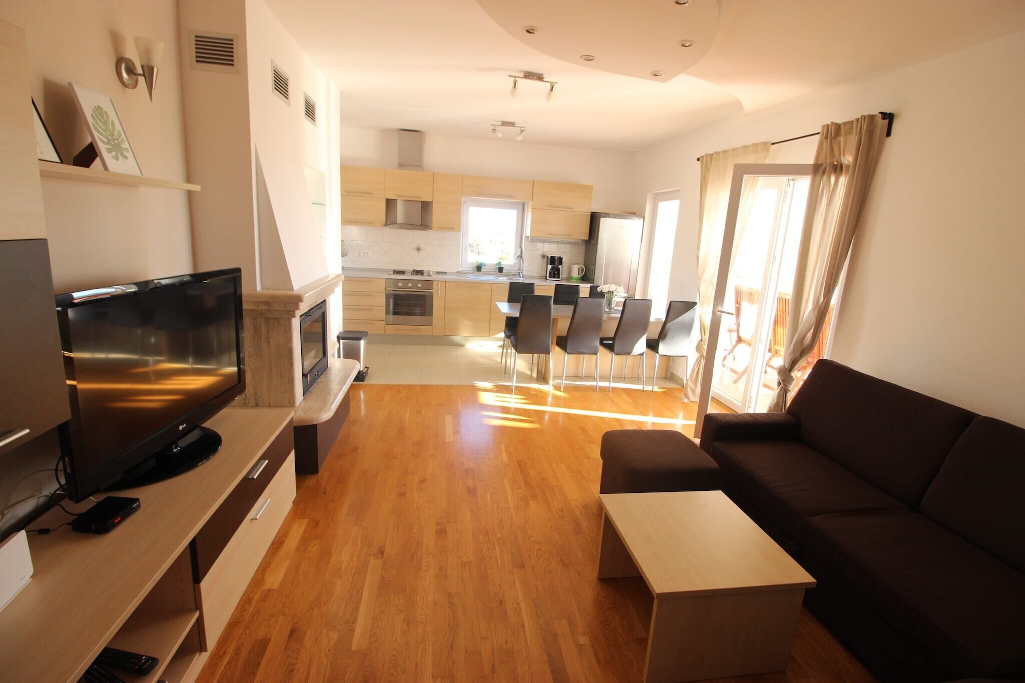 Una sala de estar moderna con televisor de pantalla plana, piso de madera, un sofá y un comedor con sillas y una mesa.