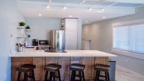 A modern kitchen with a large island, stainless steel appliances, and wooden bar stools. - Recent remodel - Large 1BR w/ ocean view and walk to excellent beaches/eateries (Kihei)