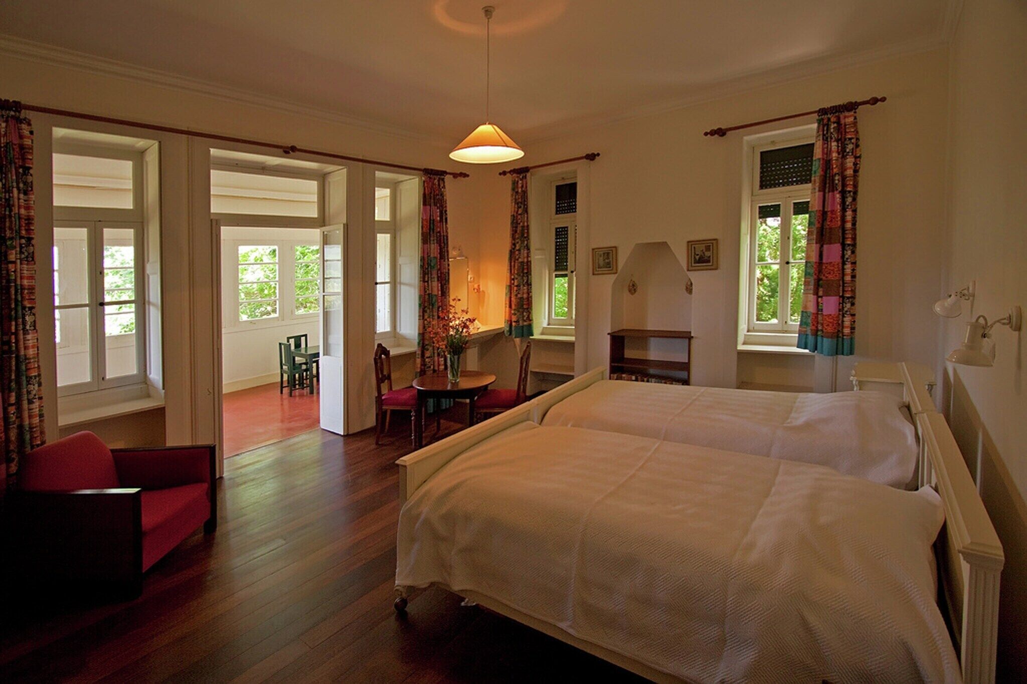 Een slaapkamer met twee bedden, een eettafel, stoelen en een raam met gordijnen.