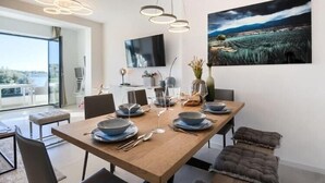 A modern dining area with a wooden table set for six, a flat-screen TV mounted on the wall, and a large landscape painting above the table. - Villa in Pula with Private Swimming Pool (Pješčana Uvala)