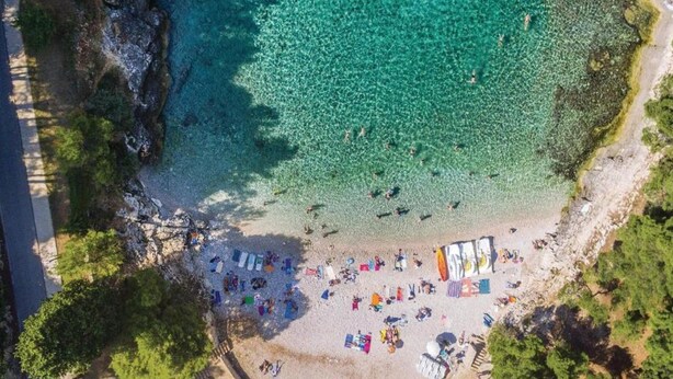 An aerial view of a beach with clear turquoise water, a sandy shore, and several colorful umbrellas and beach chairs. - Apartment in Ližnjan with Pool and Terrace (Ližnjan)