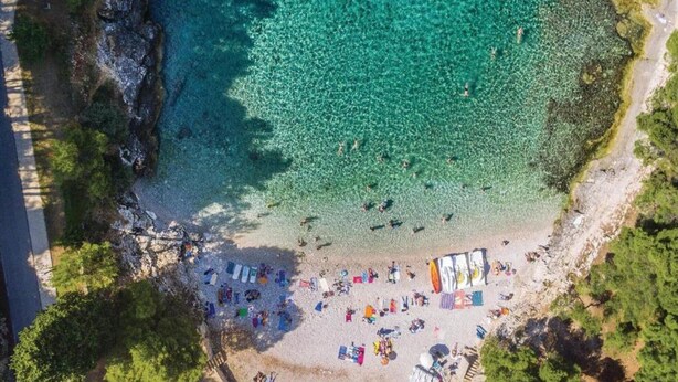An aerial view of a beach with clear turquoise water, a sandy shore, and several colorful umbrellas and beach chairs. - Apartment in Ližnjan with Pool Terrace (Ližnjan)
