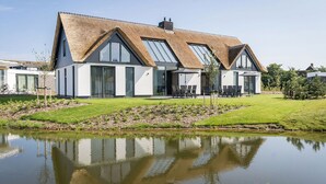 A modern house with a thatched roof, large windows, and a well-maintained lawn.