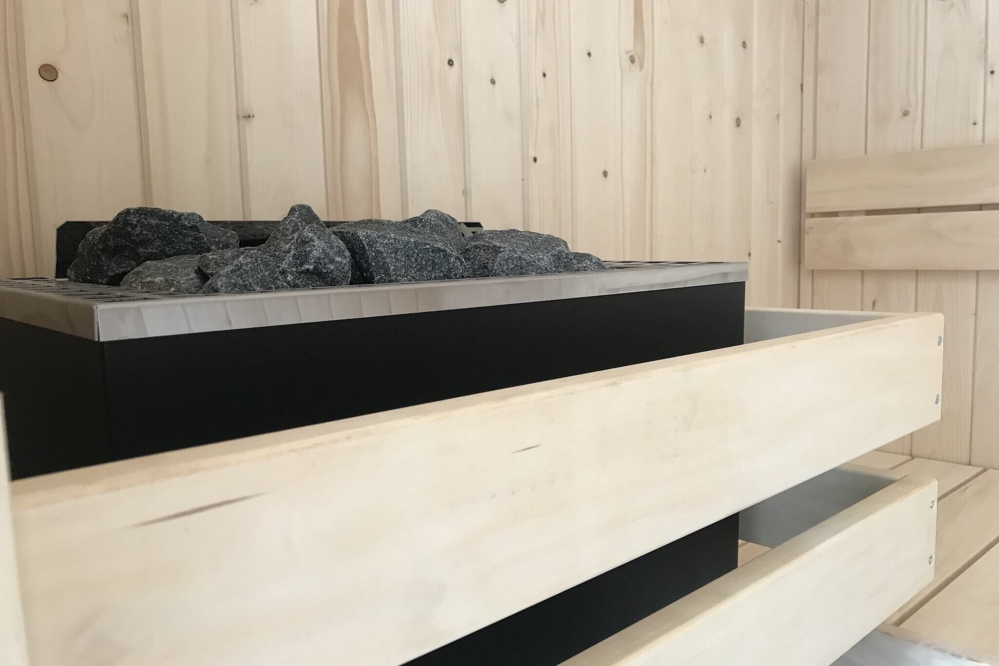 Un sauna en bois avec un bain de pierres chauffées de couleur noire.