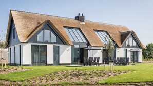 A modern house with a thatched roof, large windows, and a well-maintained lawn.