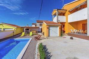 Uma área residencial com piscina, área de estar externa e um edifício de dois andares com garagem.