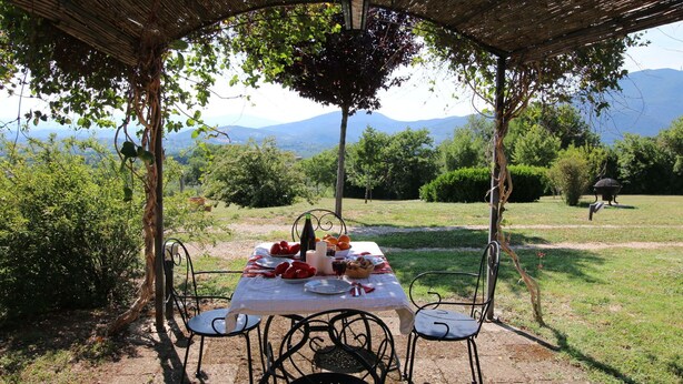 Ein Essbereich im Freien mit Tisch und Stühlen, überdacht von einer Pergola.