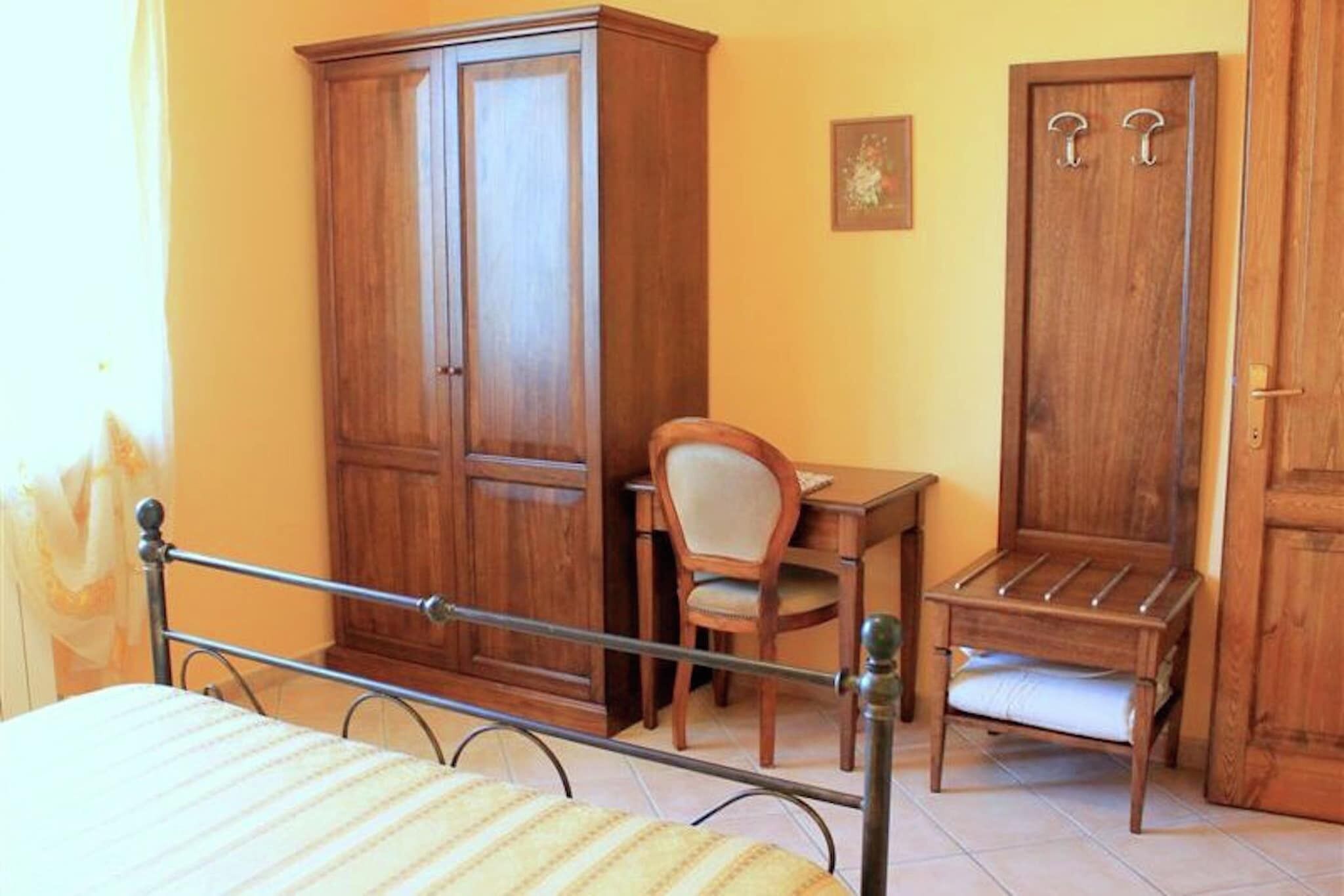 A bedroom with a bed, a wooden wardrobe, a desk with a chair, and a small wooden stool.