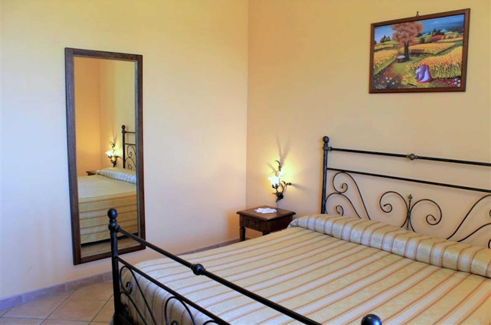 A bedroom with a bed, a nightstand, a mirror, and a painting on the wall.