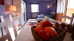 Una habitación con una mesa lista para el desayuno, una cama con colcha azul y una ventana con vistas a la vegetación.