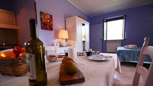 Una habitación con una mesa de comedor preparada para dos personas, una botella de vino y una cesta de naranjas.