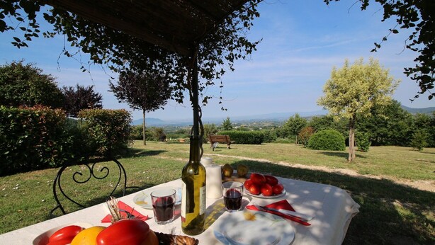 Mesa de comedor al aire libre con una botella de vino, copas y un plato de fruta.