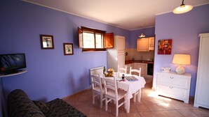 Un comedor con una mesa, sillas y un ventanal. Se observa una cocina al fondo, con armarios y encimera.